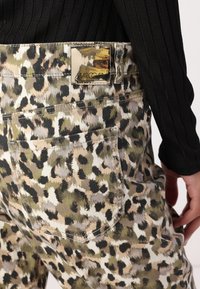 Leopardenmuster-Hosen in einer Mischung aus Grün-, Braun- und Beigetönen. Verfügt über Gesäßtaschen und ein Markenetikett am Bund. Strukturierter Stoff.