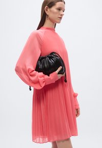 Abito corallo plissettato con maniche lunghe a palloncino. Borsa nera testurizzata con coulisse tenuta contro il corpo. Design semplice ed elegante.