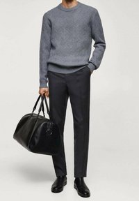 Szary sweter w splot warkoczowy, ciemne, dopasowane spodnie i czarna skórzana torba podróżna. Całość dopełniają czarne botki, podkreślające minimalistyczny design.