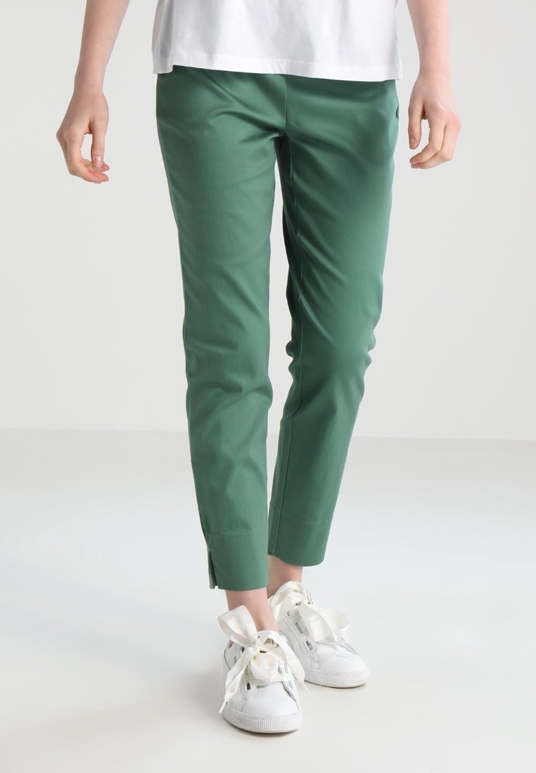 Pantalons verts ajustés en tissu lisse, avec un design épuré, de subtils fentes sur l'ourlet, associés à des baskets blanches.
