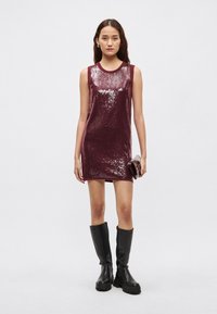 Bordové trblietavé šaty bez rukávov s okrúhlym výstrihom, doplnené čiernymi čižmami po kolená a malou čiernou kabelkou.