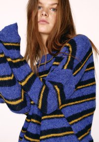 Modrý pletený sveter s horizontálnymi pruhmi v tmavomodrej a žltej farbe. Mäkká textúra, voľný strih a široké rukávy. Výrazný vzor cik‐cak.