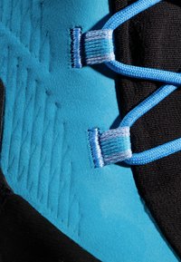 Section de chaussures de sport bleu et noir avec une texture en daim lisse, des motifs texturés et des lacets bleu clair. Présente une vue rapprochée de la quincaillerie.