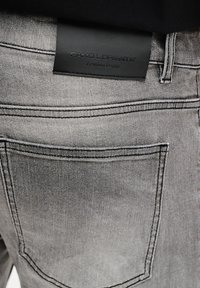 Szare dżinsy wykonane z denimu z czarną skórzaną metką z wytłoczonym napisem "Pako Lorente" i "Premium Denim". Widoczne szwy i detale kieszeni.