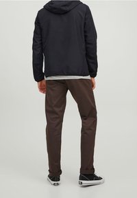 Black hooded jacket, gray shirt underneath, brown trousers, and black sneakers with white soles. Smooth material and casual design.