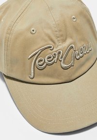 Khaki czapka baseballowa z haftowanym logo "Teen Crew" w beżu. Posiada okrągłą koronę i przeszyty daszek, z dwoma otworami wentylacyjnymi.