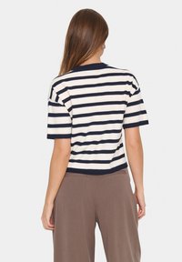 Pull rayé à manches courtes en crème et marine, avec un col rond. Texture douce avec une coupe décontractée, accompagné de pantalons beiges.