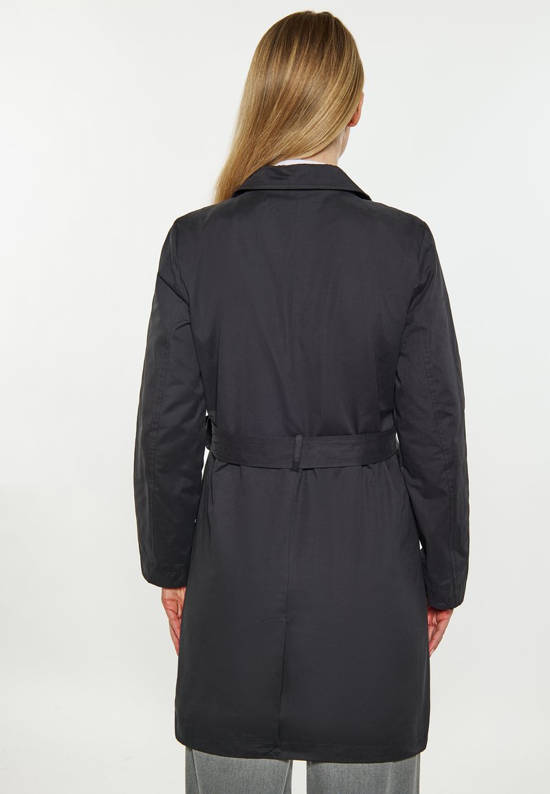 Schwarzer Trenchcoat mit tailliertem Gürtel und langen Ärmeln. Glattes Material, Kragen-Design und mittellange Schnittform. Minimalistischer Stil.
