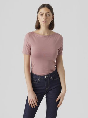 Lys rosa t-skjorte med korte ermer og rund hals, kombinert med mørkeblå jeans. Stoffet ser mykt ut og har en lett glans.