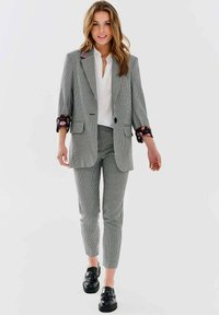 Szary marynarka w kratę z czarnymi kwiecistymi mankietami, w komplecie ze slim-fit spodniami i czarnymi loafersami. Biała koszula pod spodem.