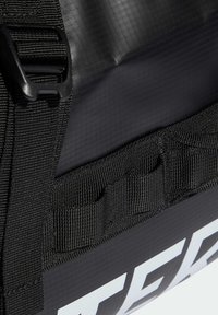 Crna vodootporna torba s teksturiranim završetkom, čvrstim crnim trakama i istaknutim bijelim logom. Sadrži sigurnosno kopčanje s kopčom.