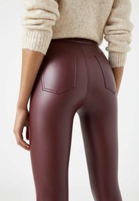 Person klädd i höga, mörkbruna läderbyxor med bakfickor och en ljusbeige stickad tröja med uppvikt ärmar.