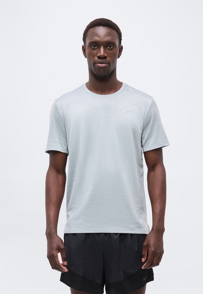 Man wearing light gray short-sleeve athletic shirt and black shorts, standing against a plain white background.