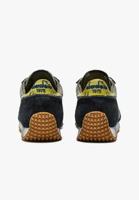 Zapatillas de ante y malla en gris y azul marino, con un acento amarillo en el talón, suela texturizada y entresuela blanca en contraste.