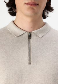 Light beige knit polo with a classic collar and short zipper at the neck. Soft texture with minimal pattern and subtle stitching details.