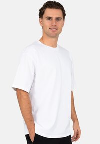 Witte, kortemouwen t-shirt van katoen. Heeft een ronde halslijn en een relaxte pasvorm, gedragen met handen in de zakken van zwarte broek.