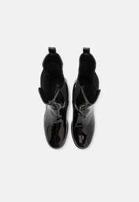 Bottines noires en cuir verni avec une finition brillante, des panneaux latéraux élastiques et des languettes pour les tirer. Texture lisse et design élégant et moderne.