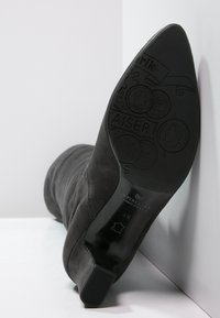 Bottine en daim noir avec une tige texturée, un bout effilé et une semelle noire lisse présentant des motifs embossés et des détails de marque.