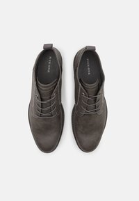 Chaussures en cuir gris foncé avec un design à lacets, bout arrondi et surface texturée. Présente un tirant et un détail de couture contrasté.