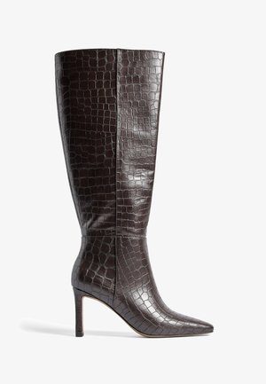 Brūni līdz ceļiem augsti zābaki, izgatavoti no krokodila raksta ādas, ar smailu purngalu un šauru stiletto papēdi. Gluda tekstūra ar spīdīgu apdari.