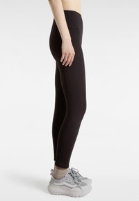 Svarta leggings med hög midja, med kontrasterande sömmar och en slät, elastisk textur, tillsammans med grå träningsskor.