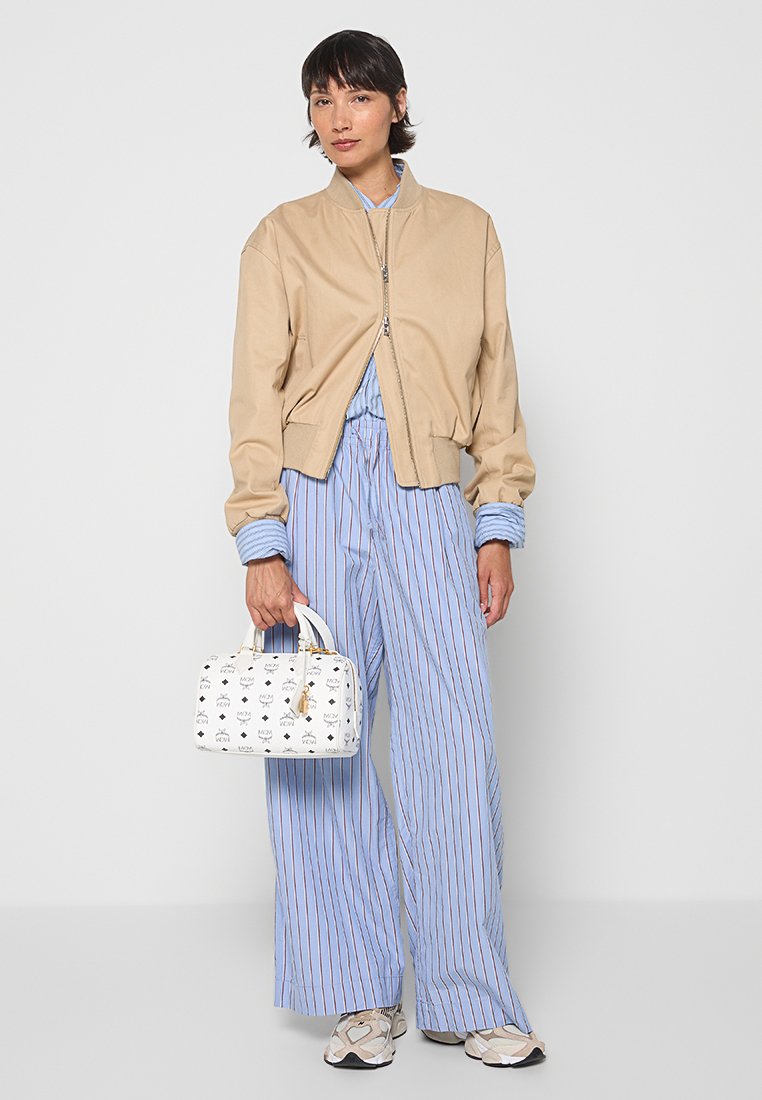 Beige Bomberjacke, hellblaue gestreifte Bluse, weit geschnittene blaue Hose, weiße Handtasche mit schwarzem Muster und graue Sneaker.