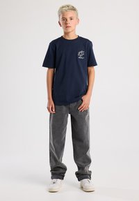 Navy cotton t-shirt with short sleeves and a small graphic on the chest, paired with loose-fitting gray jeans and white sneakers.