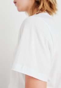Witte katoenen t-shirt met korte mouwen. De stof lijkt zacht met een gladde textuur. De zoom heeft een subtiele gestikte afwerking.