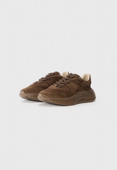 Bruna mockaskor med en strukturerad yta, med en beige insida, cirkulära perforeringar och tjocka gummisulor. Snördesign.