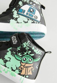Schwarze High-Top-Sneaker mit grünen Spritzermustern, die R2-D2 und einen Cartoon-Yoda zeigen. Weiße Sohle mit strukturiertem blau-grünen Laufsohlen.