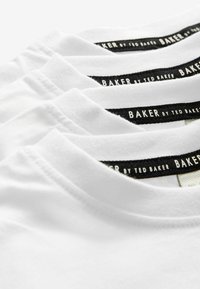 T-shirts en coton blanc empilés avec des étiquettes noires portant l'inscription "BAKER by TED BAKER", présentant des encolures rondes et une texture lisse.