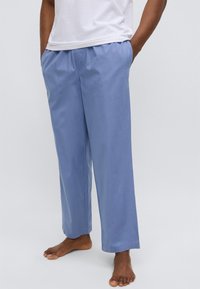 Lyseblå bomullsbukser med elastisk liv, sidelommer og en avslappet passform. Jevn tekstur og rett snitt ned til anklene.