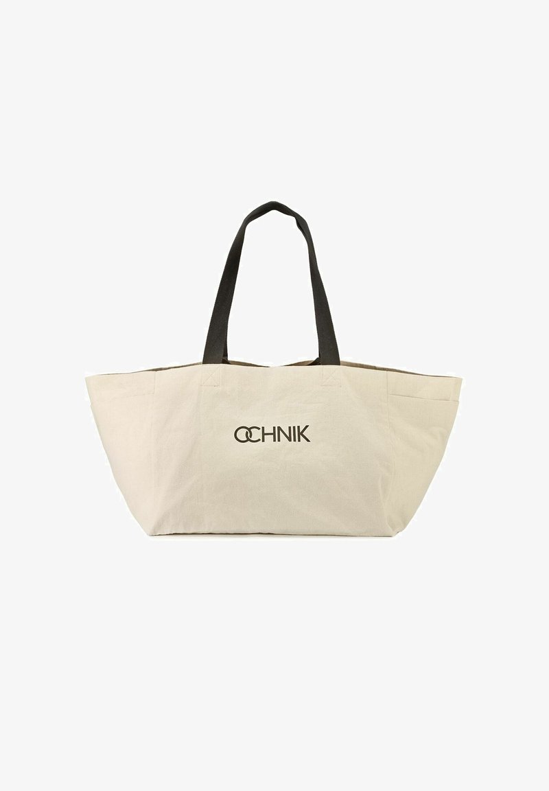 Beżowa torba na ramię z płótna z czarnymi uchwytami, z delikatnym fałdem na górze, z nadrukowanym na czarno słowem "OCHNIK".