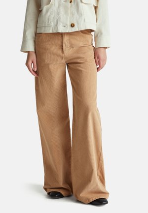 Lichte tan corduroy wijd-uitlopende broeken met een gestructureerd oppervlak, voorzakken en een ontspannen pasvorm. Gecombineerd met een crèmekleurige cropped jas.