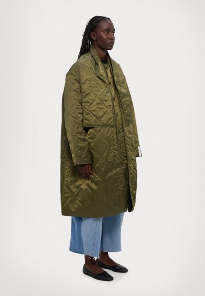Olivově zelený prošívaný oversized kabát s vysokým límcem a knoflíkovým zapínáním, v kombinaci s širokými zkrácenými denimovými džíny a černými balerínami.
