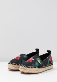 Espadrillas negras con un patrón floral que presenta flores rojas y hojas verdes. Suela de cuerda de yute y parte superior de tela negra, con dos tiradores.