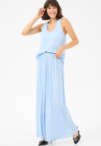 Robe maxi sans manches bleu clair avec une coupe décontractée et une taille froncée. Le tissu fluide descend jusqu'au sol, complété par des chaussures noires.