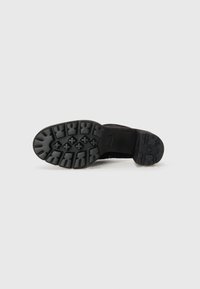 Black rubber boot sole with a textured, multi-directional tread pattern. Features raised accents and grooves for grip and durability.