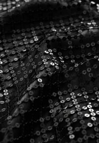 Tissu noir pailleté présentant un motif en grille de petits sequins ronds sur une base lisse, créant une surface texturée et réfléchissante.