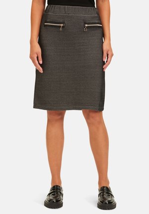Falda de patrón blanco y negro hasta la rodilla con dos bolsillos delanteros con cremallera, combinada con mocasines negros y una blusa negra.