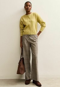 Cardigan giallo lavorato a maglia con motivo a trecce, bottoni verdi. Pantaloni a gamba larga in plaid grigio. Borsa marrone e scarpe marroni completano l'outfit.