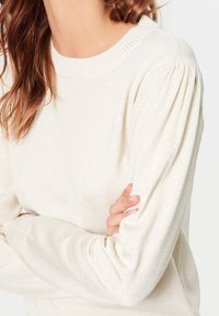 Jasno beżowy sweter dzianinowy z prążkowanym, okrągłym dekoltem i długimi, bufiastymi rękawami, z subtelnym połyskiem i miękką teksturą.