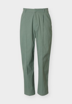 Pantalon vert fuselé avec passants de ceinture et plis avant, présenté sur un fond clair uni.