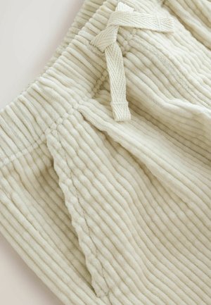 Light beige pants with a textured, ribbed fabric feature a drawstring waistband, showcasing soft and cozy material details.