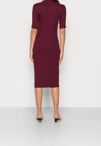Abito midi aderente bordeaux con maniche corte e scollo alto, realizzato in tessuto liscio. Presenta una lunghezza sotto il ginocchio e cuciture minime.