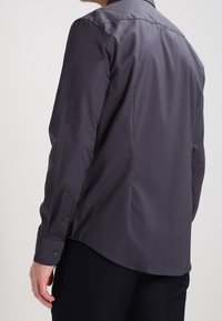 Camicia a maniche lunghe grigio scuro con una texture liscia, polsini buttonati e orlo curvo, dotata di un colletto classico e design con yoke posteriore.