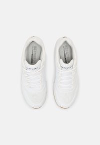 Zapatillas deportivas blancas con parte superior de malla texturizada, perforaciones para la transpirabilidad, collarete acolchado y suela de goma. Presenta un logo en la lengüeta.