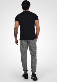 Camiseta negra de manga corta combinada con pantalones de chándal gris jaspeado, con corte slim y puños acanalados, completada con zapatillas negras.
