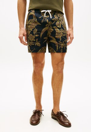 Herre sorte shorts med brun tropisk bladprint og hvid snøre, kombineret med brune læder snørestøvler og olivengrøn skjorte.