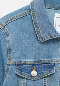 Giacca di jeans azzurro chiaro con colletto classico, due tasche sul petto con accessori in argento e dettagli di cucitura gialla a contrasto.